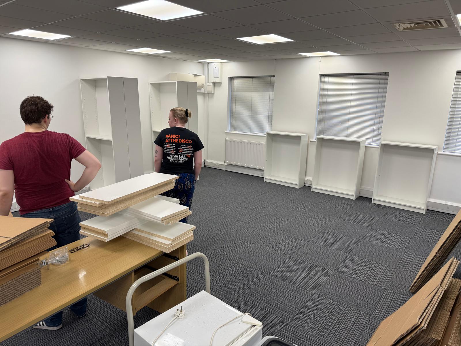 Guy and Milly among half-built bookcases and flat-packed shelves in the newly moved-into Marlow office